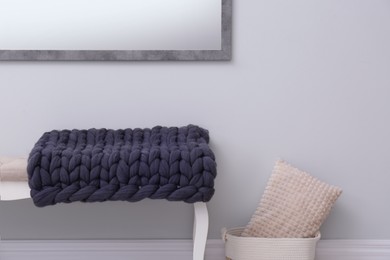 Knitted merino wool plaid on bench near grey wall