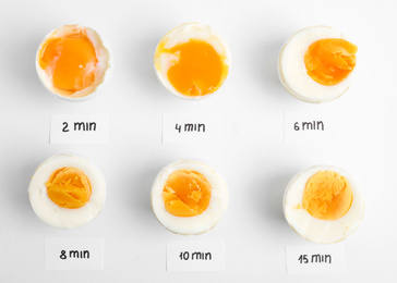 Photo of Different cooking time and readiness stages of boiled chicken eggs on white background, flat lay