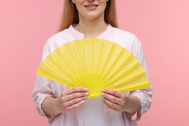 Woman with yellow hand fan on pink background, closeup