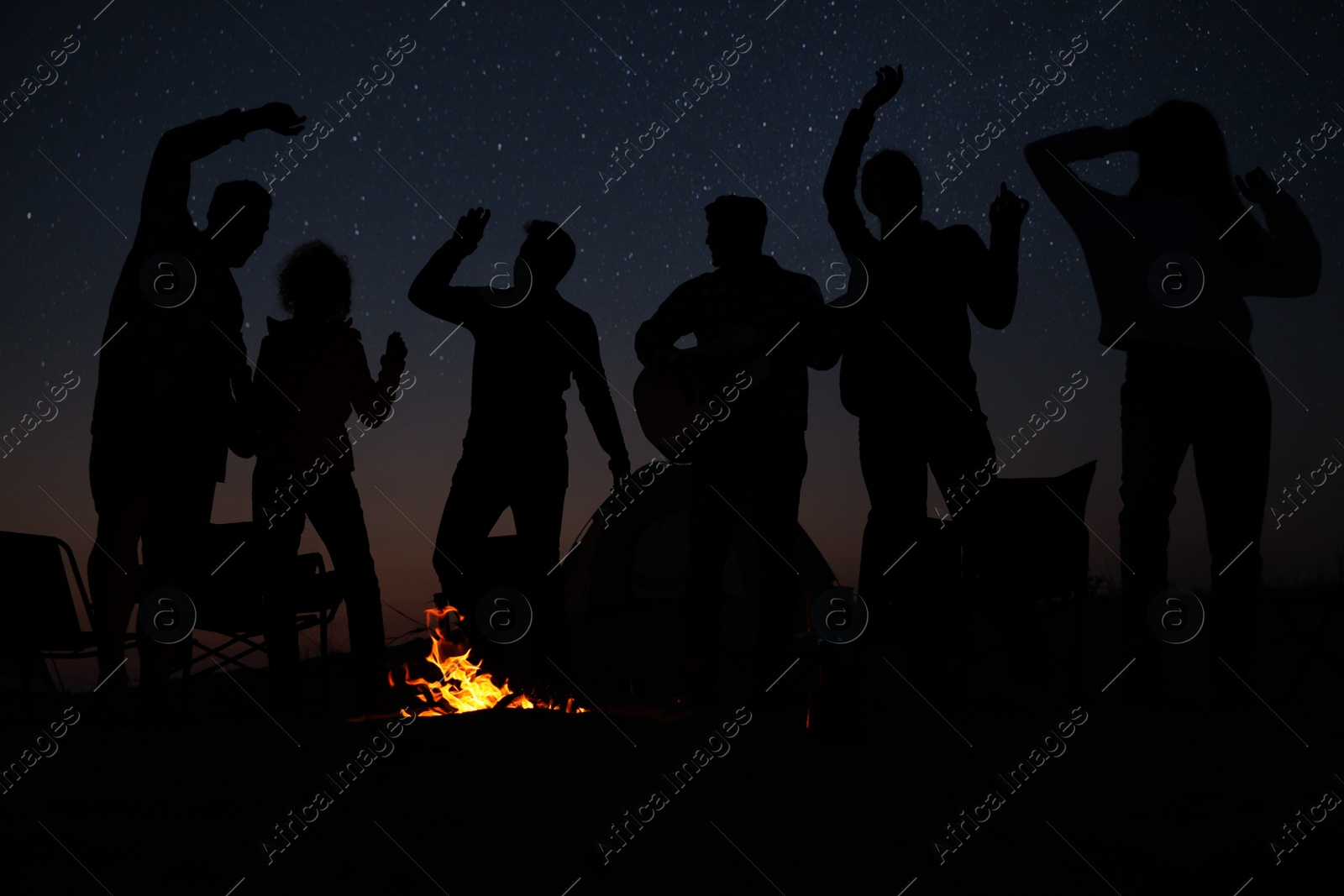 Photo of Group of friends having party near bonfire at night. Camping season