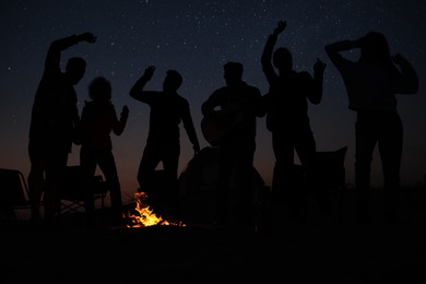 Photo of Group of friends having party near bonfire at night. Camping season