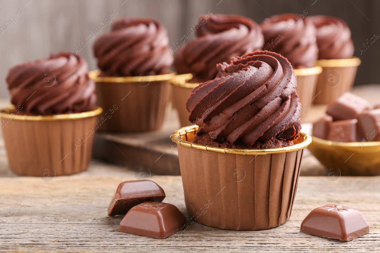 Photo of Delicious cupcakes and chocolate pieces on wooden table, closeup