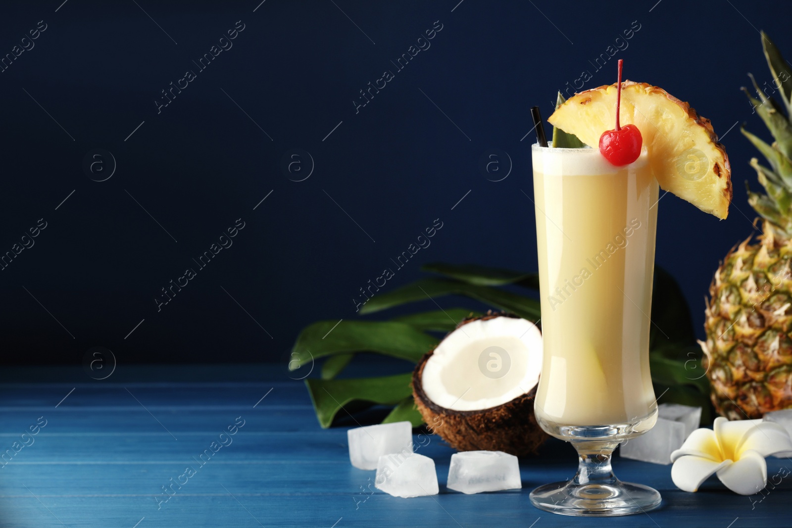 Photo of Tasty Pina Colada cocktail and ingredients on blue wooden table, space for text