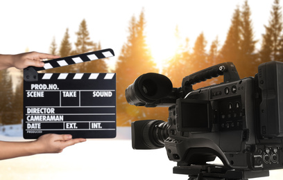 Image of Modern video camera and assistant with clapperboard outdoors, closeup. Cinema production 