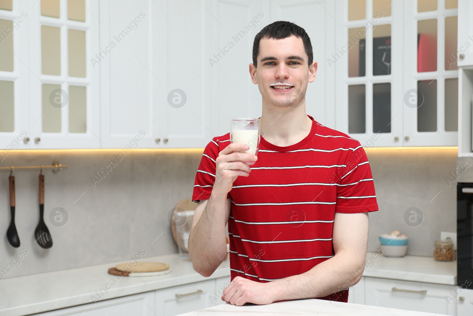 Photo of Happy man with milk mustache holding glass of tasty dairy drink in kitchen