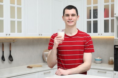 Happy man with milk mustache holding glass of tasty dairy drink in kitchen