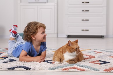 Photo of Happy little boy and cute ginger cat on carpet at home