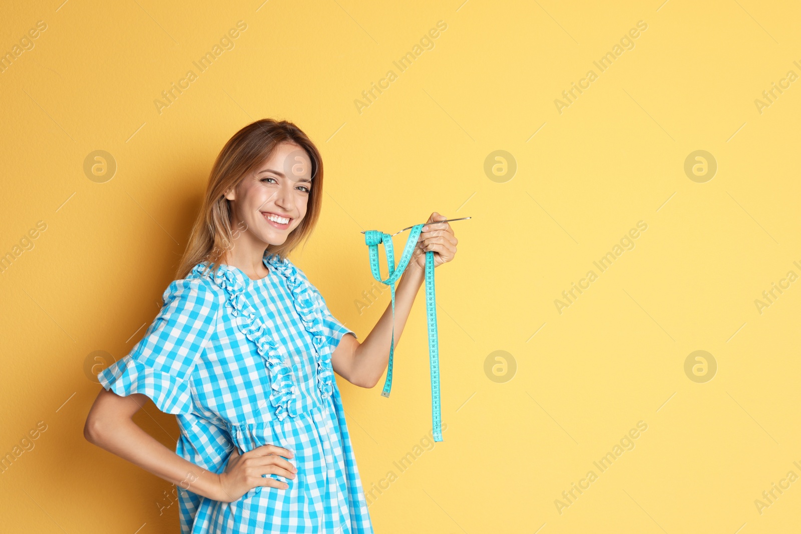 Photo of Happy young woman holding fork with measuring tape on color background. Weight loss diet