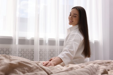 Beautiful woman sitting on bed at home, space for text. Lazy morning