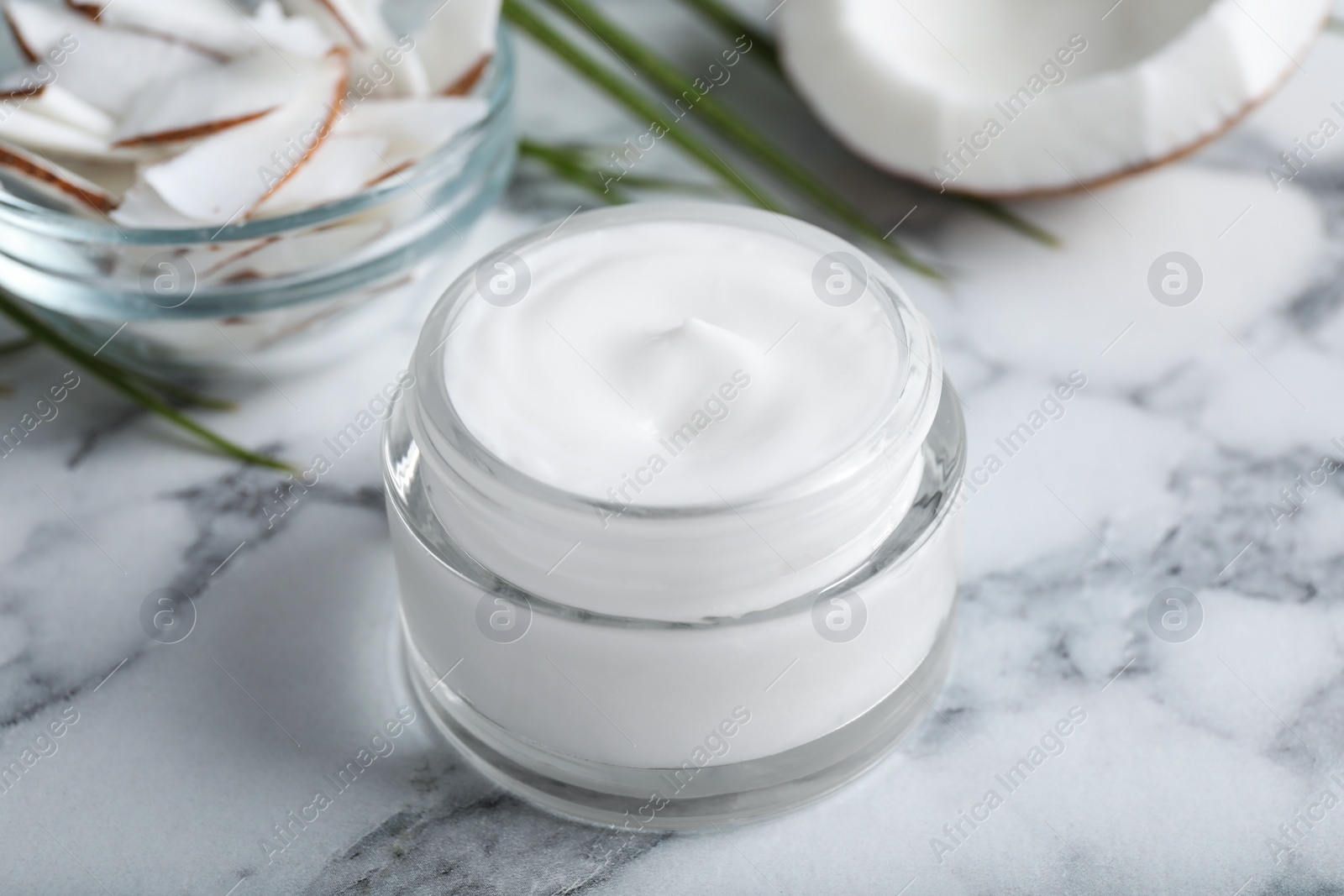 Photo of Jar of body cream with coconut on white marble table, closeup