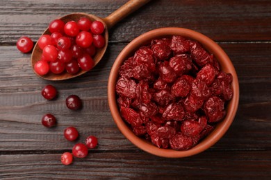 Photo of Tasty dried cranberries in bowl and fresh ones on wooden table, top view