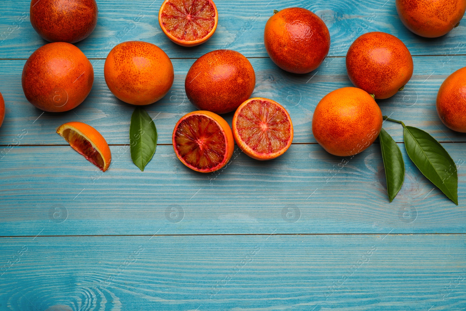 Photo of Many ripe sicilian oranges and leaves on light blue wooden table, flat lay. Space for text