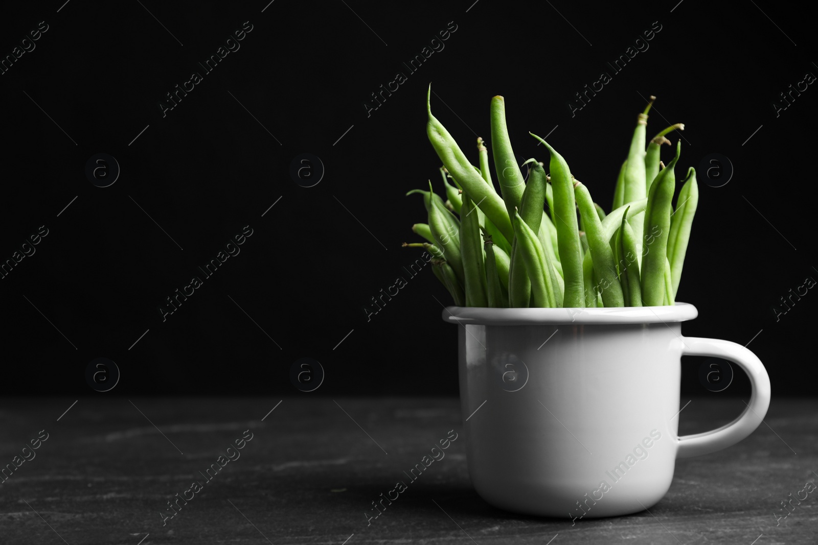 Photo of Fresh green beans in white mug on black table, space for text