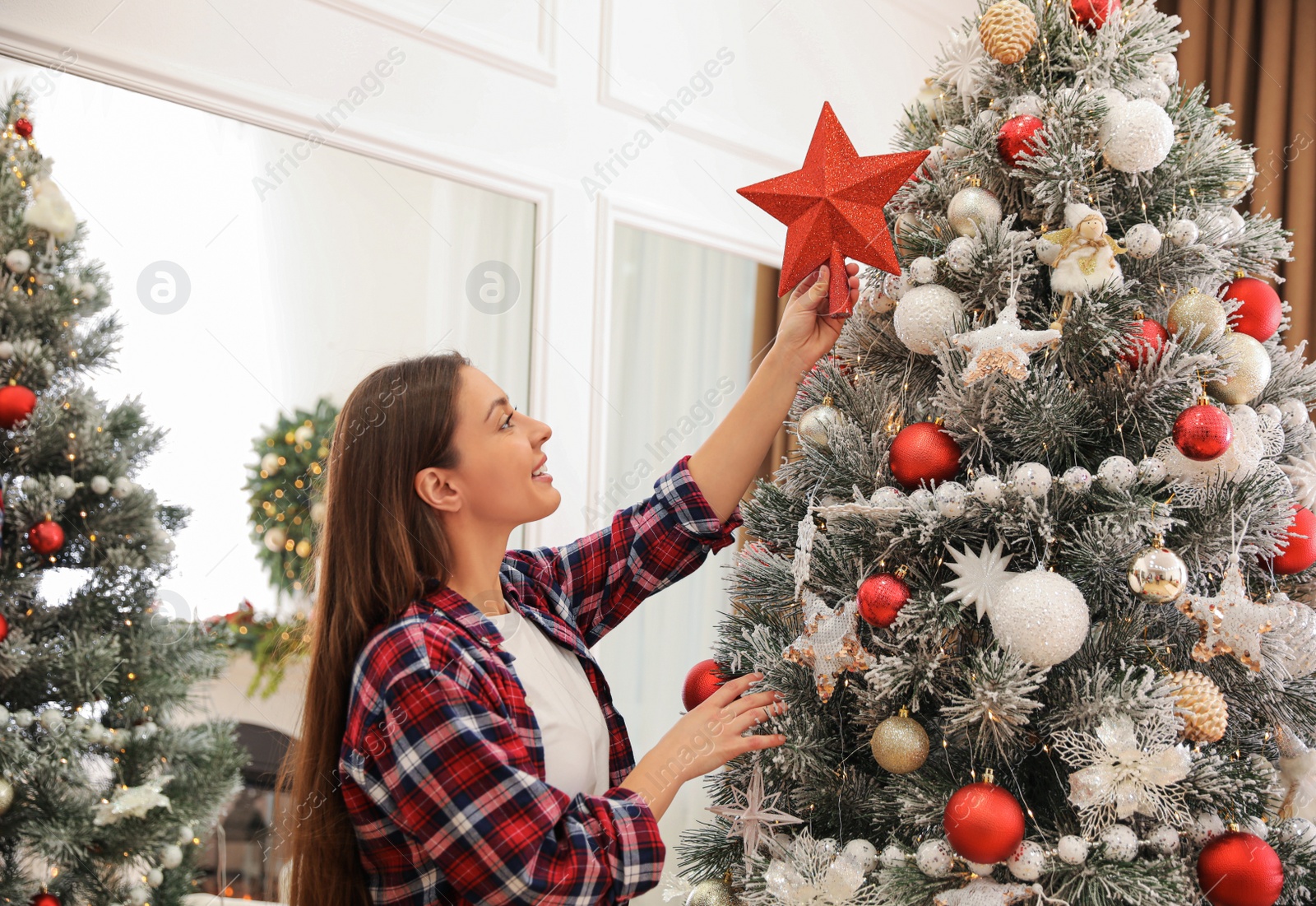 Photo of Woman decorating Christmas tree with star topper indoors