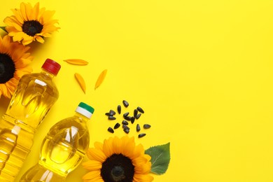 Bottles of cooking oil, sunflowers and seeds on yellow background, flat lay. Space for text