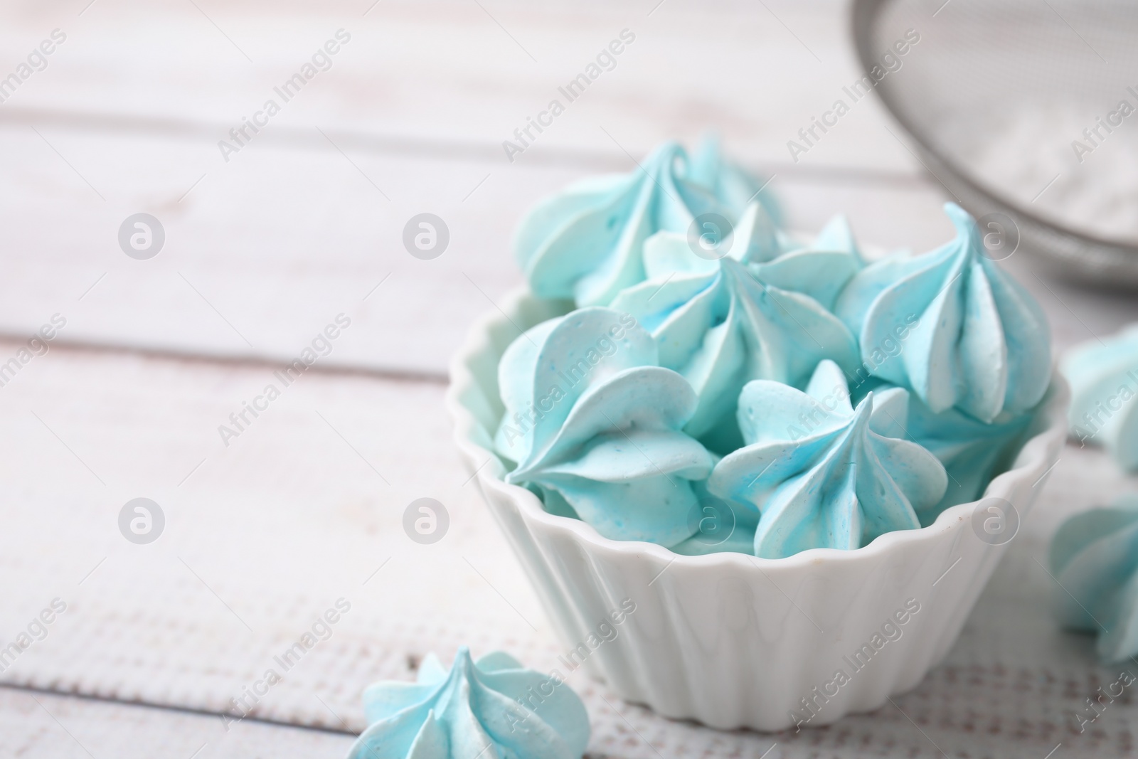 Photo of Tasty meringue cookies in bowl on white wooden table. Space for text