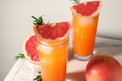 Photo of Tasty grapefruit drink with ice in glasses, rosemary and fresh fruits on light table, closeup