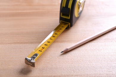 Photo of Self retracting metal measuring tape and pencil on wooden table, closeup