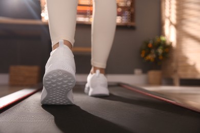 Photo of Sporty woman training on walking treadmill at home, closeup