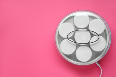 Modern yogurt maker with jars on pink background, top view. Space for text