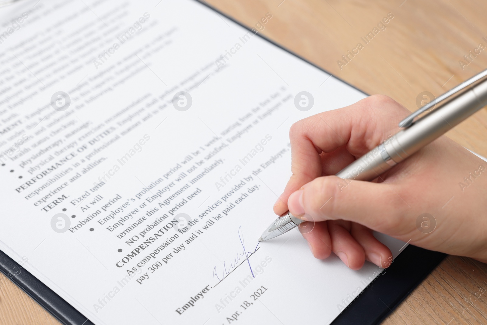 Photo of Woman signing contract at wooden table, closeup.