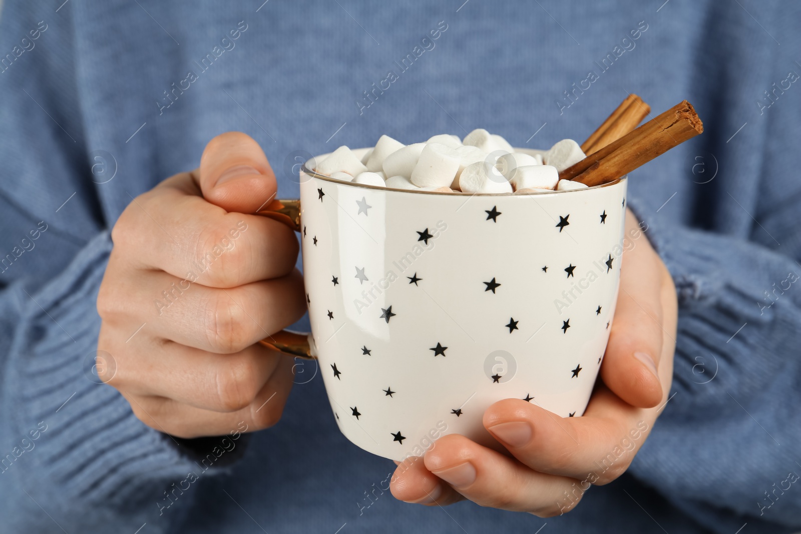 Photo of Woman holding cup of delicious hot chocolate with marshmallows and cinnamon sticks, closeup