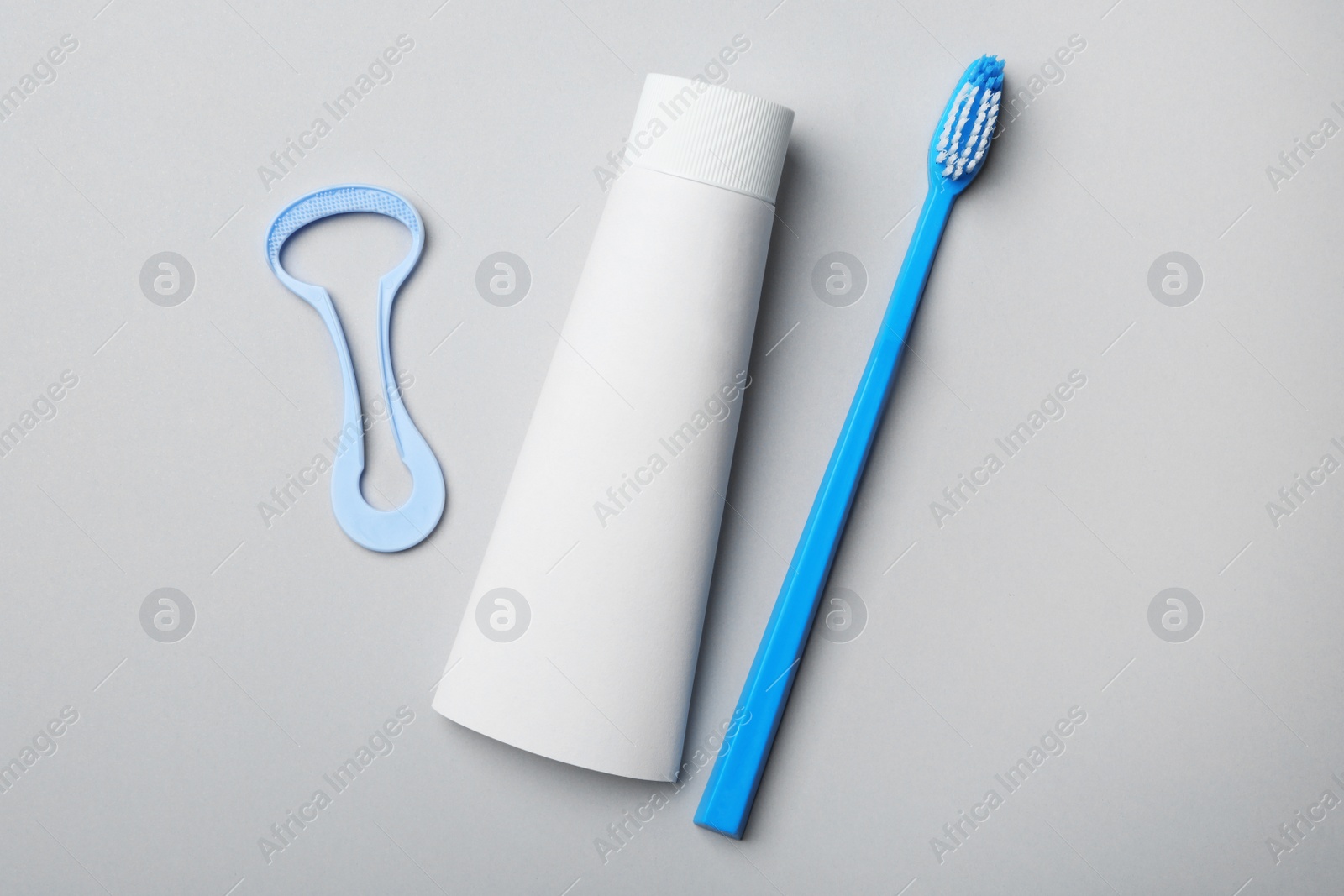 Photo of Tongue cleaner, tooth paste and brush on grey background, flat lay