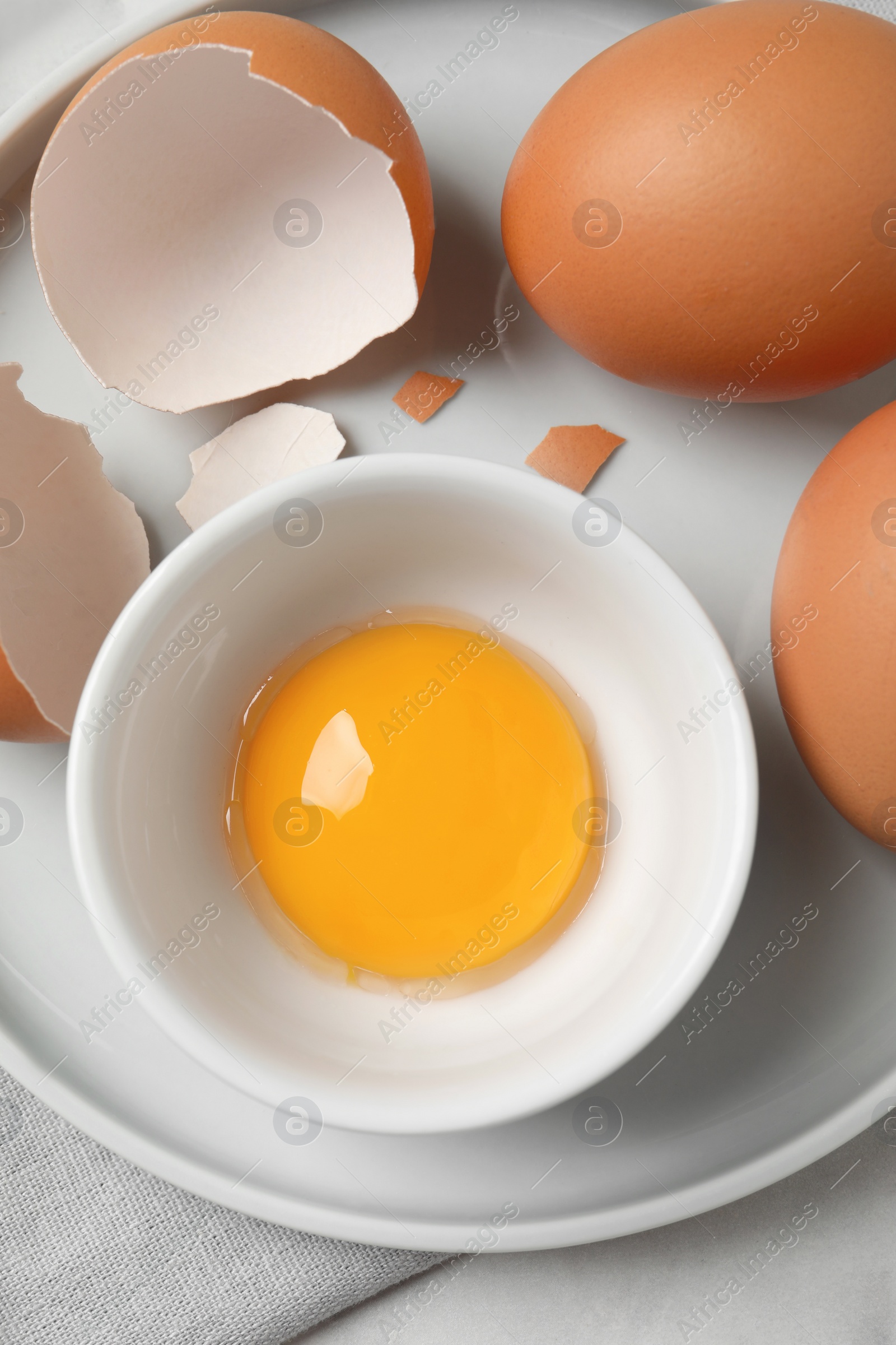 Photo of Chicken eggs and bowl with raw yolk on table, top view