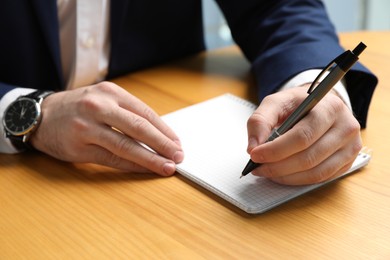 Photo of Left-handed man writing in notebook at wooden desk, closeup