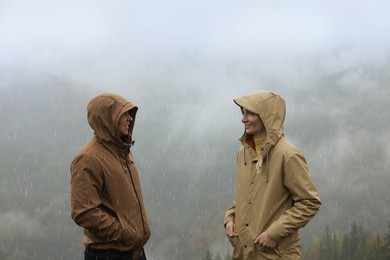 Photo of Man and woman in raincoats talking outdoors during rain