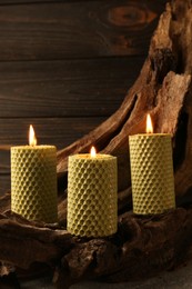 Photo of Beautiful burning beeswax candles on snag near wooden wall