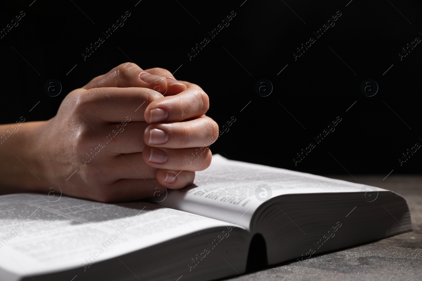 Photo of Religion. Christian woman praying over Bible at table against black background, closeup. Space for text