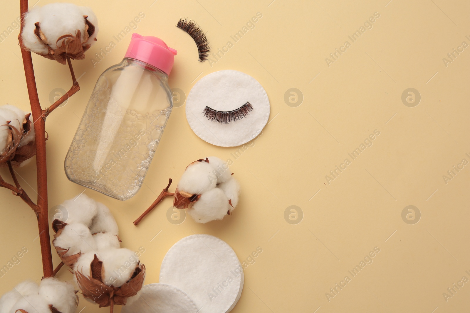 Photo of Bottle of makeup remover, cotton flowers, pads and false eyelashes on yellow background, flat lay. Space for text
