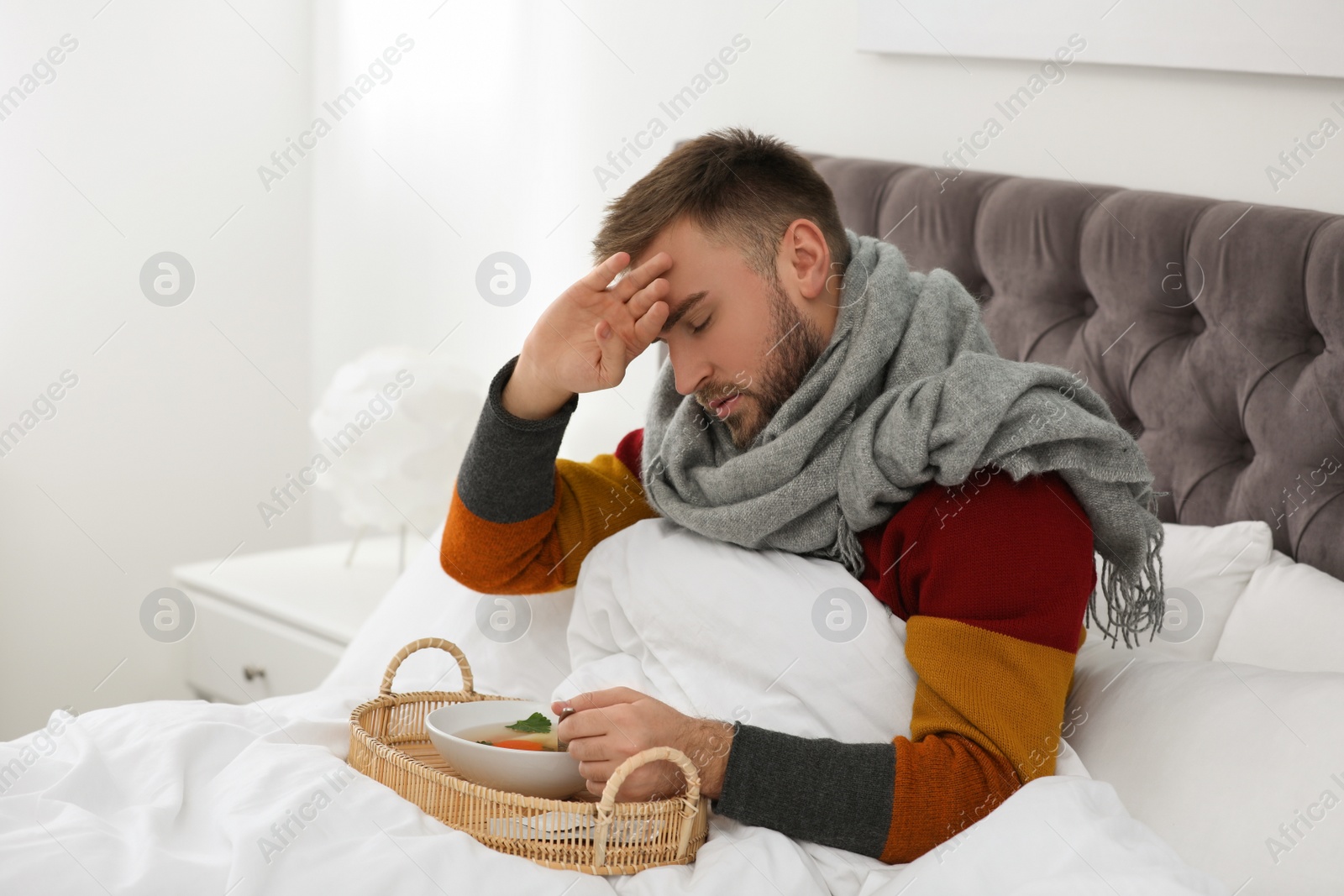 Photo of Sick young man with bowl of tasty soup in bed at home