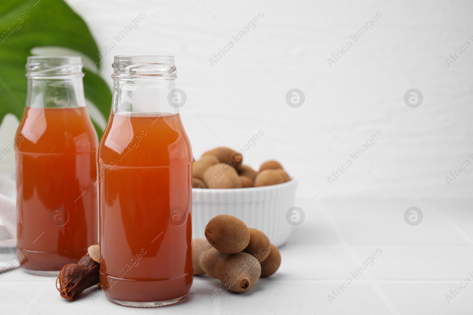 Photo of Tamarind juice and fresh fruits on white tiled table, space for text