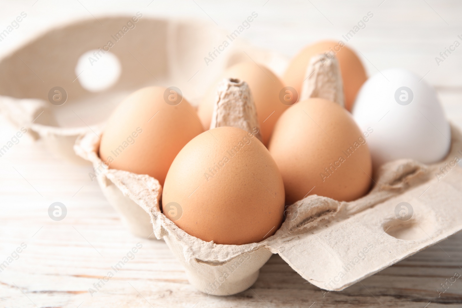 Photo of Carton of raw chicken eggs on wooden background, closeup