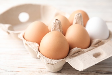 Photo of Carton of raw chicken eggs on wooden background, closeup