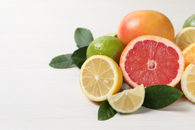 Different cut and whole citrus fruits on white wooden table, closeup. Space for text