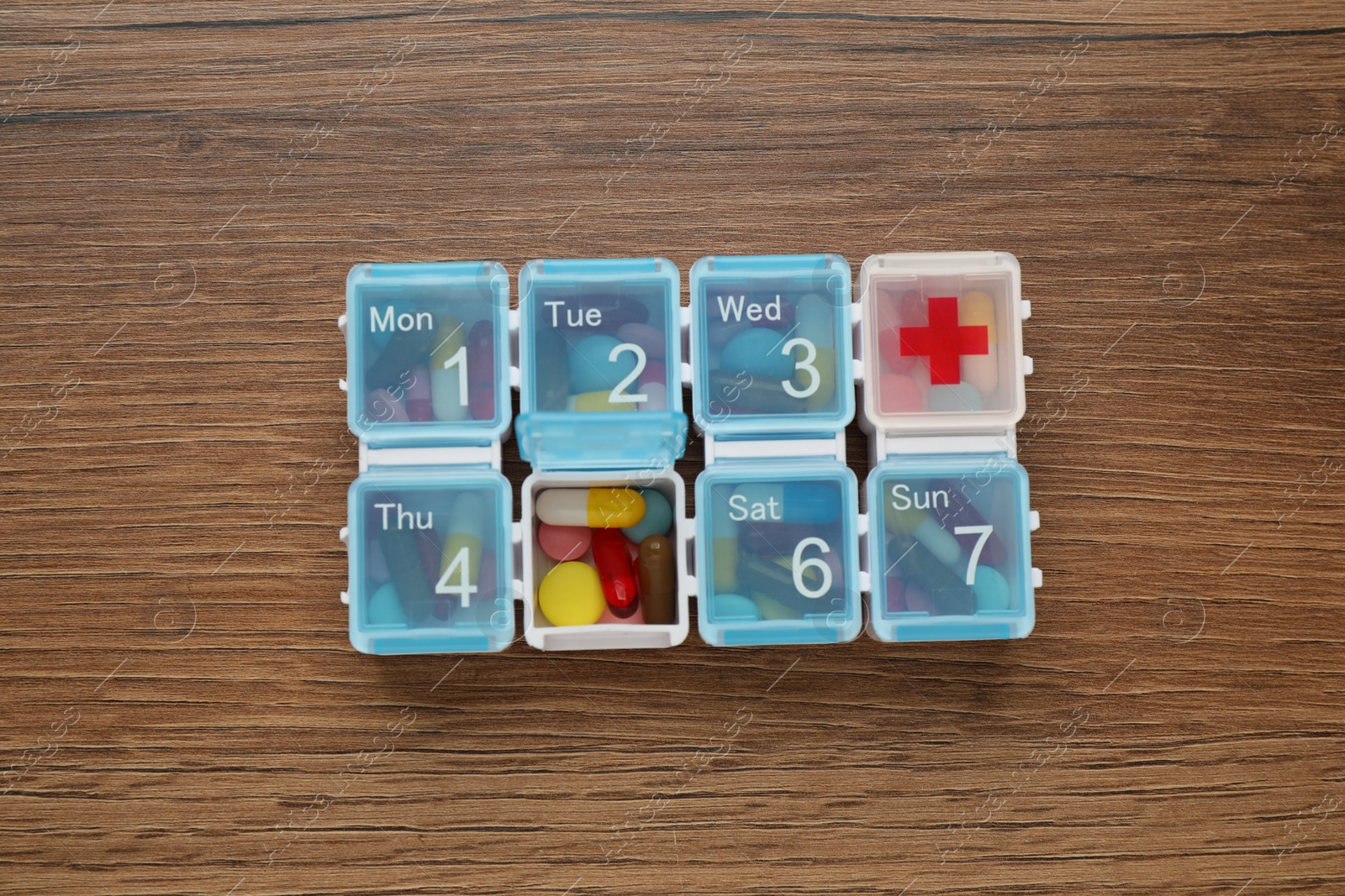 Photo of Plastic box with different pills on wooden table, top view