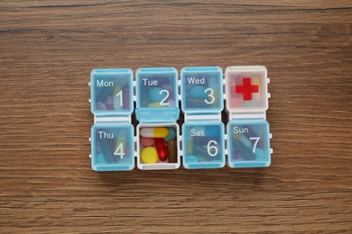 Photo of Plastic box with different pills on wooden table, top view