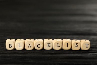 Photo of Cubes with word Blacklist on black wooden table, closeup
