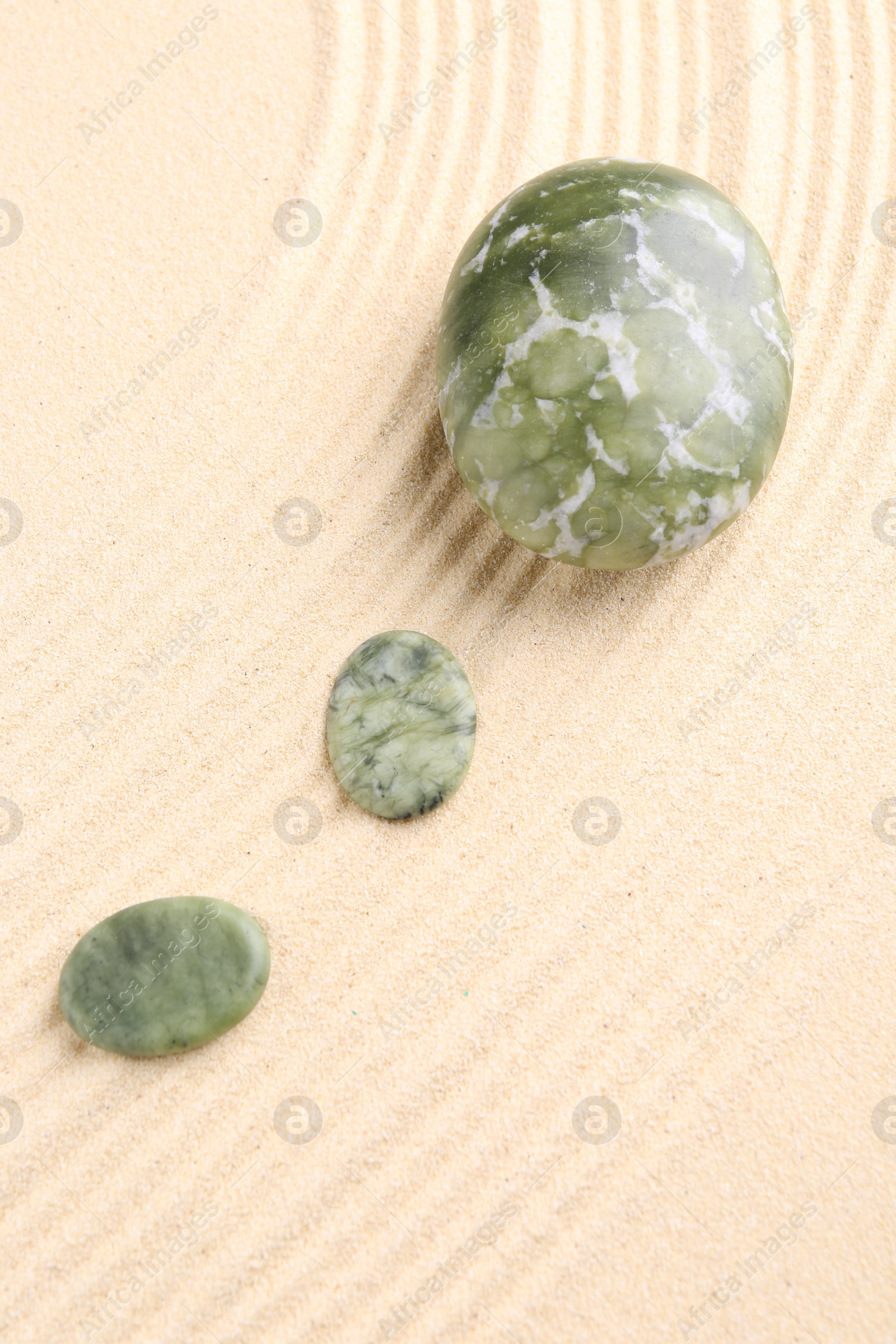 Photo of Zen garden stones on beige sand with pattern, flat lay