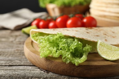 Photo of Tasty homemade tortilla, lettuce, lime and tomatoes on wooden table, closeup