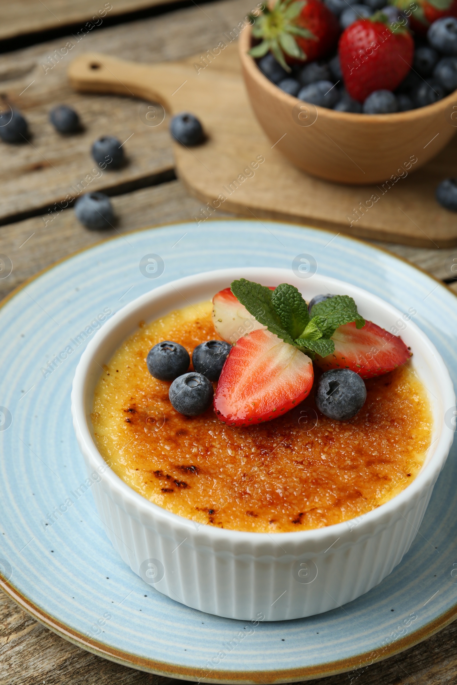 Photo of Delicious creme brulee with berries and mint in bowl on wooden table, closeup