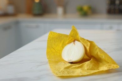 Photo of Half of onion with yellow beeswax food wrap on white marble table, space for text