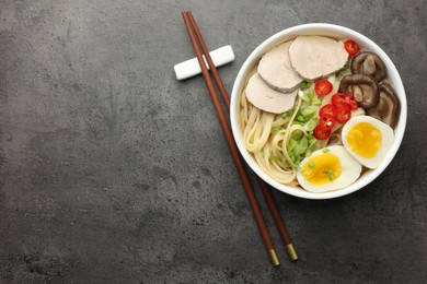 Photo of Delicious ramen with meat in bowl and chopsticks on grey textured table, top view. Space for text. Noodle soup