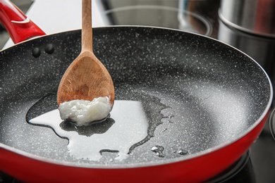 Photo of Wooden spoon with coconut oil in frying pan. Healthy cooking