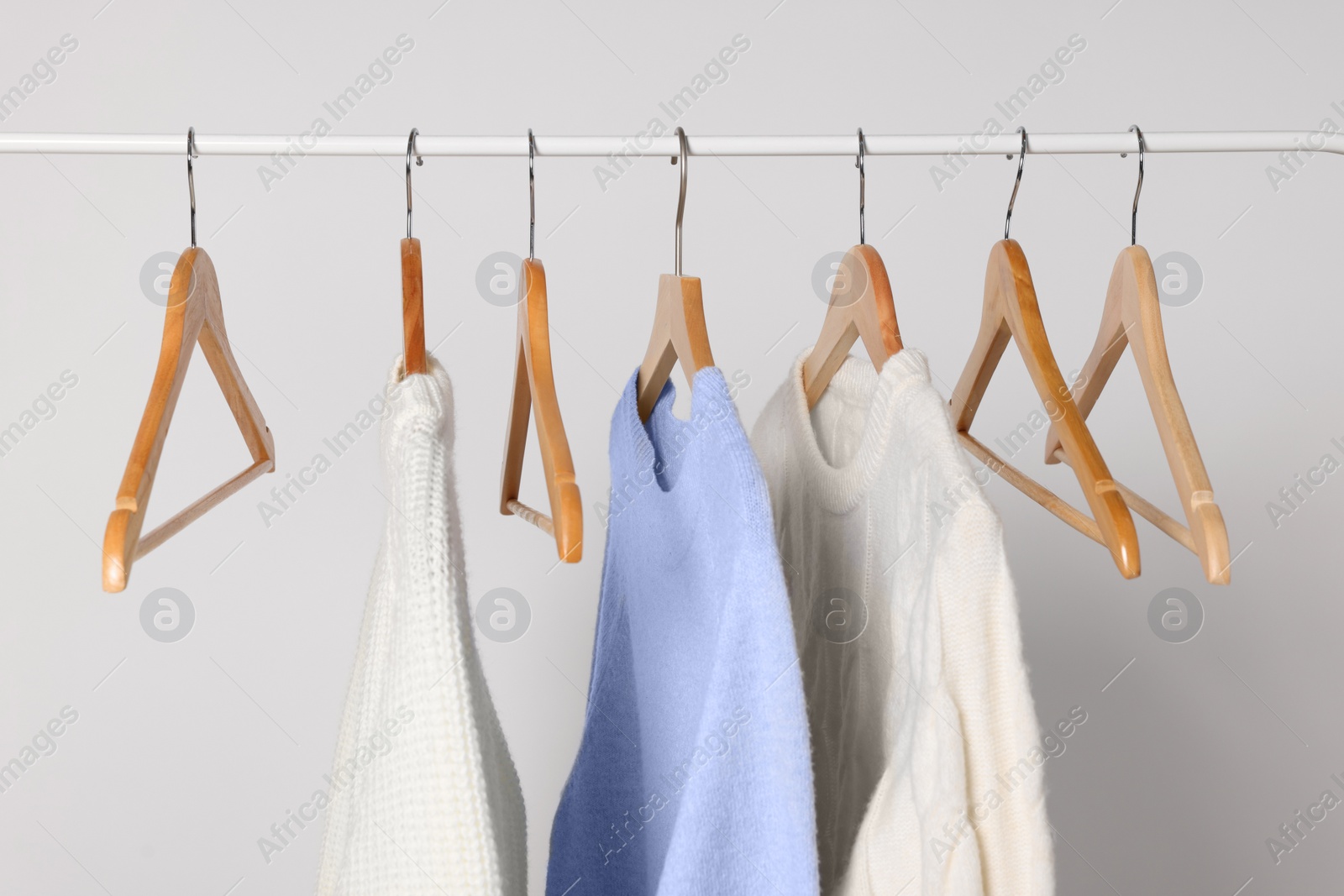 Photo of Rack with different warm sweaters on light background