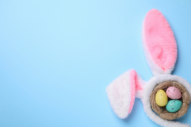 Photo of Headband with bunny ears, painted eggs and space for text on light blue background, flat lay. Easter holiday