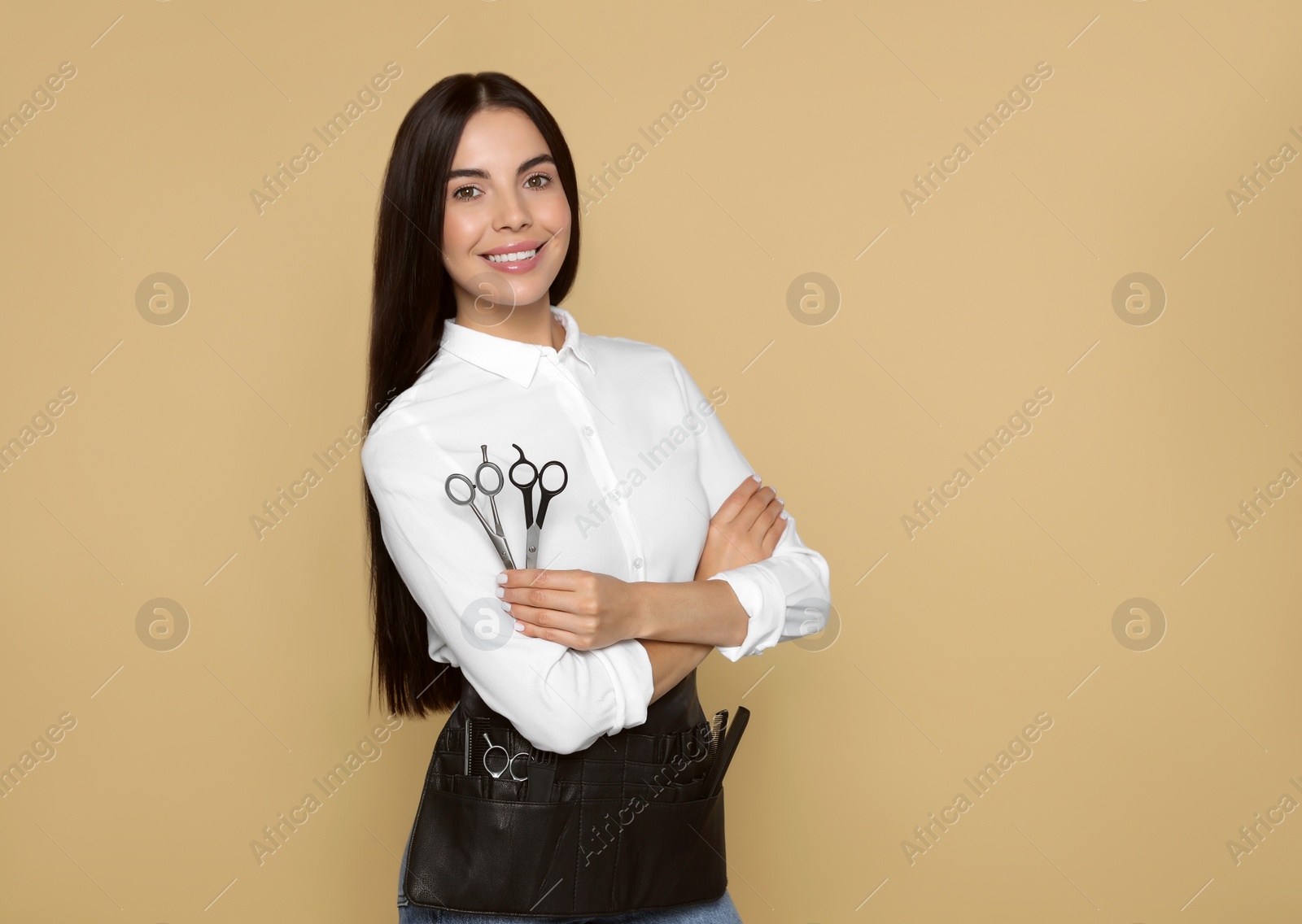 Photo of Portrait of happy hairdresser with professional scissors on beige background, space for text